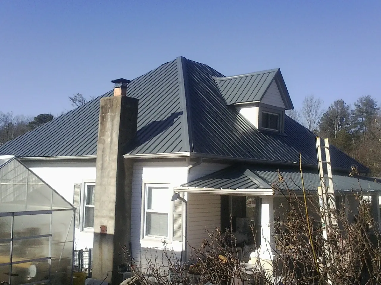Dark blue standing seam metal roof on a white farmhouse with dormer — Slate & Tile Roof Repair by Roofing Brothers in Redford