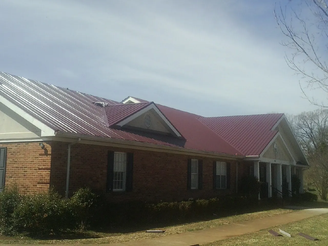 Red metal roof with gabled entries on a long brick building, from a Hail Damage Roof Repair job in Redford