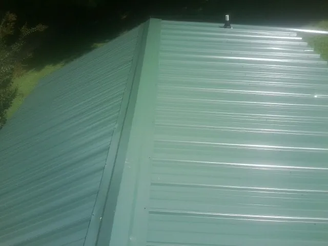 New green metal panels meeting at the ridge of a roof — Flat Roof Repair work by our crew in Redford