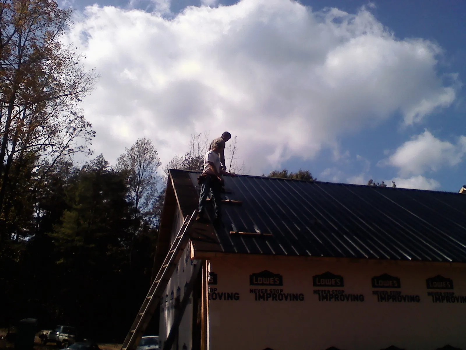 Roofer fastening dark metal panels high against a cloudy sky, from a Roof Inspection job in Redford
