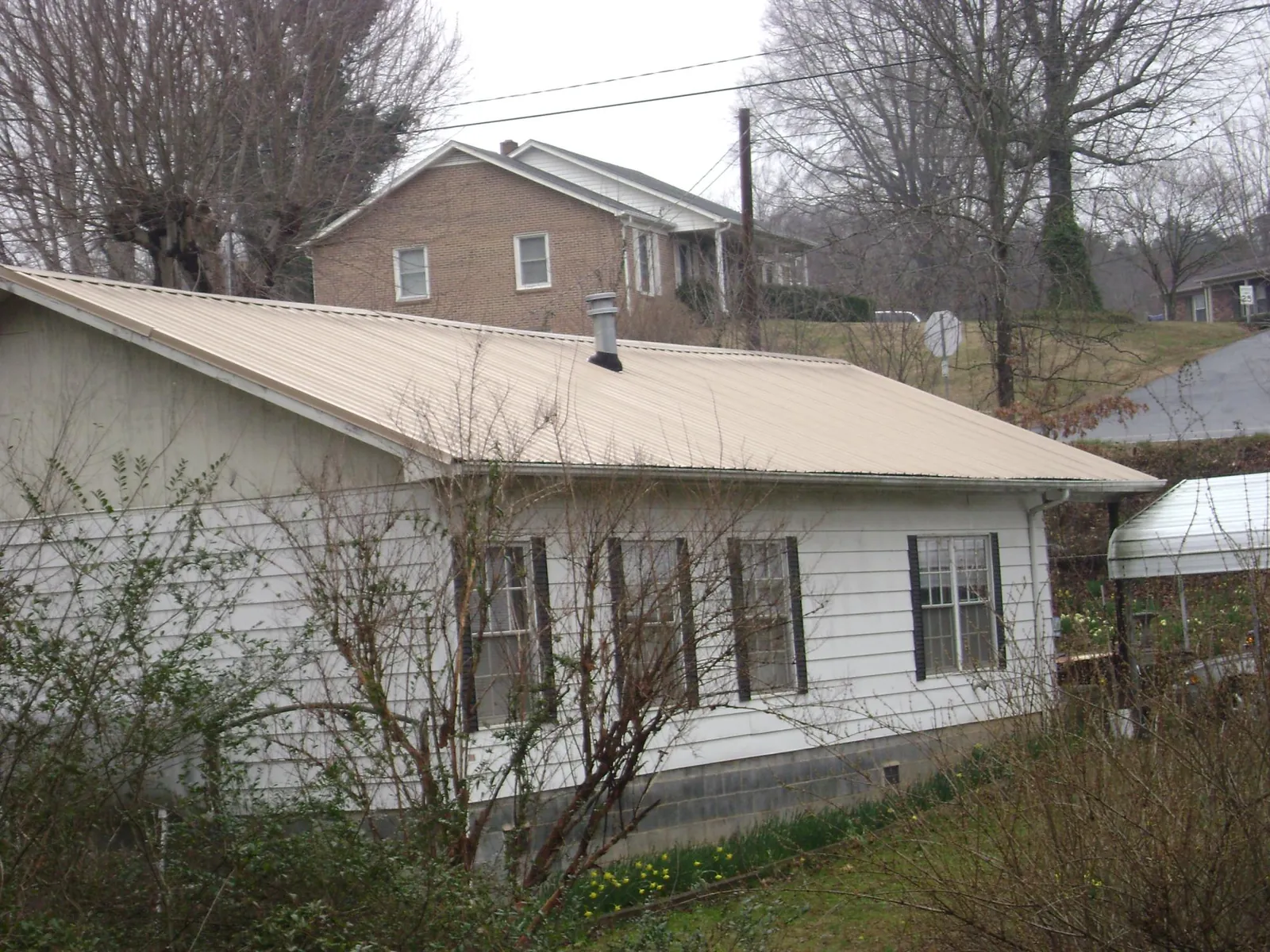 Tan metal roof on a white sided house set into a hillside — Commercial Roofing by Roofing Brothers in Redford