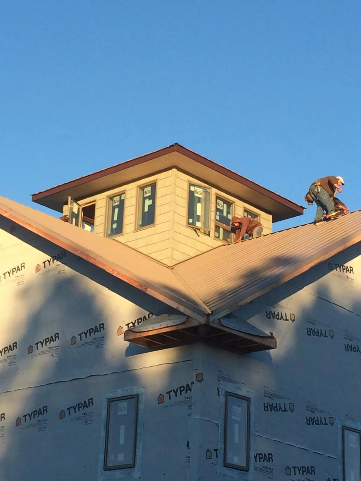 Roofers working around a rooftop cupola on a new metal roof at sunset — Roof Waterproofing in Redford by Roofing Brothers